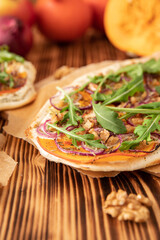 gebackener Flammkuchen mit Kürbis vom Hokkaido, Apfel, Zwiebelringen, Walnüssen, Frischkäse, Schmand, Rosmarin und Rucola auf einem Tisch aus Holz in der Küche