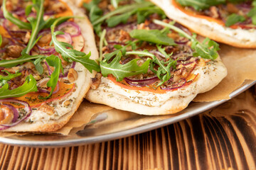 gebackener Flammkuchen mit Kürbis vom Hokkaido, Apfel, Zwiebelringen, Walnüssen, Frischkäse, Schmand, Rosmarin und Rucola auf einem Tisch aus Holz in der Küche