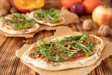 gebackener Flammkuchen mit Kürbis vom Hokkaido, Apfel, Zwiebelringen, Walnüssen, Frischkäse, Schmand, Rosmarin und Rucola auf einem Tisch aus Holz in der Küche