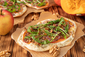 gebackener Flammkuchen mit Kürbis vom Hokkaido, Apfel, Zwiebelringen, Walnüssen, Frischkäse, Schmand, Rosmarin und Rucola auf einem Tisch aus Holz in der Küche