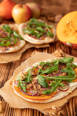 gebackener Flammkuchen mit Kürbis vom Hokkaido, Apfel, Zwiebelringen, Walnüssen, Frischkäse, Schmand, Rosmarin und Rucola auf einem Tisch aus Holz in der Küche