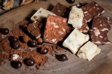 Composition of bars and pieces of different milk and dark chocolate, grated cocoa on a brown background top view close up.