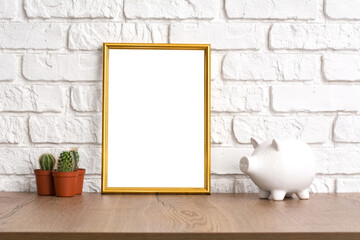 Mockup blank golden frame with place for text or image, cactus and piggy bank on wooden table. Work place concept.
