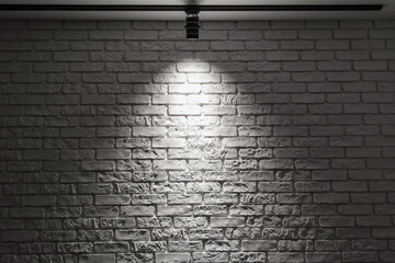 White brick wall with track light. Spotlight beam on the wall. Dark background.
