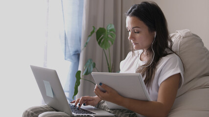 Young woman wears headset conference calling on laptop talks with online teacher studying, working from home. Lady student learning using computer webcam chat makes notes. Distance education concept