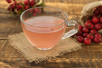 Rosehip tea in a glass cup close-up on a wooden table. In the background are rose hips and a bag of berries. Shallow depth of field.