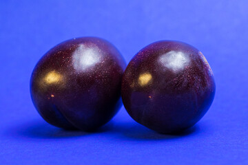 Unusual associations. Two ripe plums together on blue background
