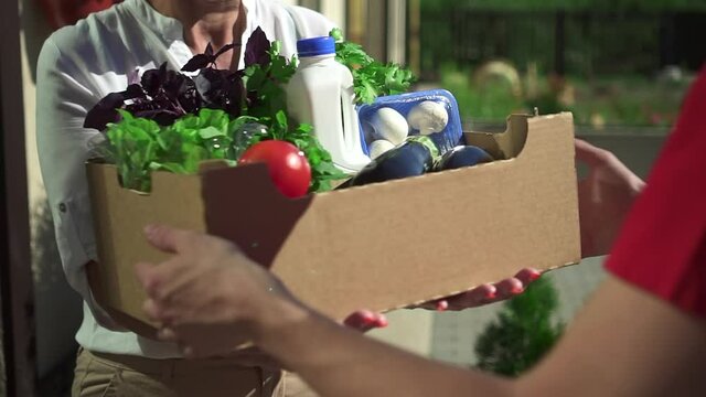 Delivery man give box with food to client woman closeup. Spbd senior woman receive donation from volunteer. Vegetables grocery. Service, supermarket, pandemic concept.