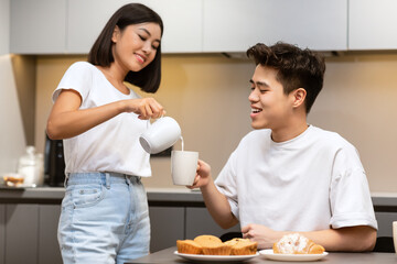 Obraz na płótnie Canvas Wife Adding Milk To Husband's Coffee During Breakfast In Kitchen