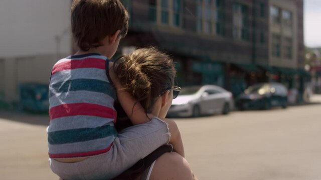 A young boy sits on his mom's shoulders as they walk down a city street