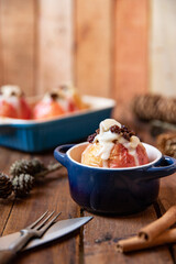 gebackener Bratapfel mit Füllung aus Marzipan, Mandeln, Rosinen und Zimt mit Vanillesoße zur Winterzeit und Weihnachten auf einem braunen Tisch aus Holz in der Küche