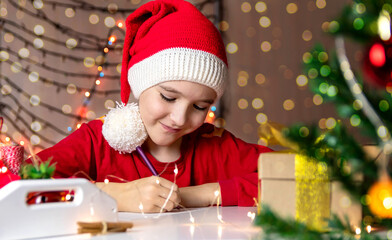 Boy in a red Christmas hat writes a letter to Santa Claus
