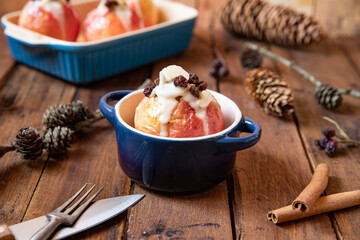 gebackener Bratapfel mit Füllung aus Marzipan, Mandeln, Rosinen und Zimt mit Vanillesoße zur Winterzeit und Weihnachten auf einem braunen Tisch aus Holz in der Küche