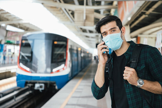 Handsome businessman wearing surgical face mask against novel coronavirus or corona virus disease (Covid-19) and using smartphone at public sky train station. Relax and listening music on the way.