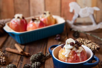 gebackener Bratapfel mit Füllung aus Marzipan, Mandeln, Rosinen und Zimt mit Vanillesoße zur Winterzeit und Weihnachten auf einem braunen Tisch aus Holz in der Küche