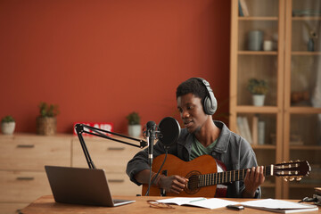 Wide angle portrait of talented African-American man singing to microphone and playing guitar while...