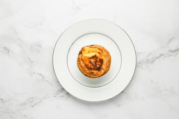 A picture of freshly baked egg tart on white plate at marble table. Famous Macao, Malaysia and Portugal snack food.