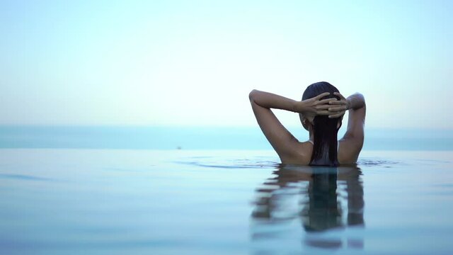 Young woman emerges from infinity pool. Slow-motion