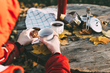 Female hiker in red jacket  having breakfast outdoor. Hot tea and biscuit  on cold morning in late...