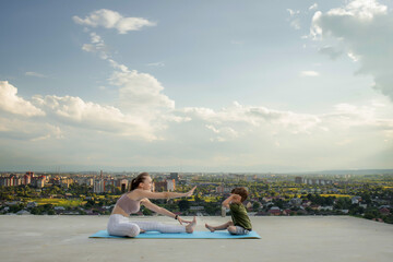 Mother and son doing exercise on the balcony in the background of a city during sunrise or sunset, concept of a healthy lifestyle