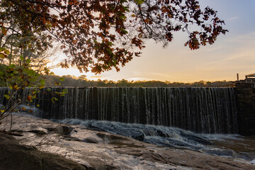 Water rushes over the edge of Yates Mill pond onto rocks in Raleigh, North Carolina at sunset in autumn