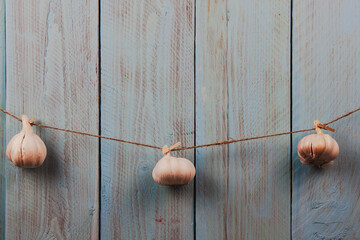 Three whole heads of garlic hanging on the rope on a blue rustic wooden background
