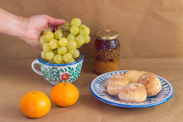 Woman's hand catching a grape cluster surrounded by some traditional Spanish cakes,  a pot of honey, tangerines presented in traditional hand-painted ceramic.