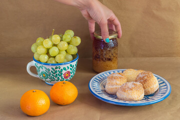 Woman's hand catching a pot of honey surrounded by some traditional Spanish cakes, grapes, tangerines presented in traditional hand-painted ceramic.