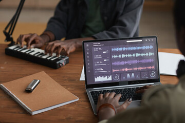 Close up of unrecognizable African-American musician using laptop with sound editing software while recording music in studio, copy space
