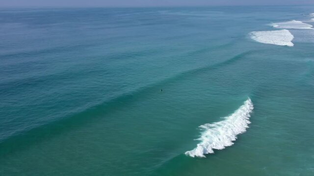 Aerial drone view of surfer sitting on his board watching the waves comming by