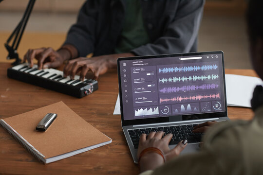 Close up of unrecognizable African-American musician using laptop with sound editing software while recording music in studio, copy space