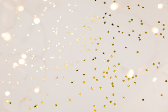 Festive gold background. Shining stars confetti and fairy lights on beige and Set Sail Champagne background. Christmas. Wedding. Birthday. Flat lay, top view, copy space
