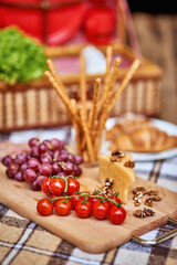 Grissini, grapes, cheese, tomatoes on wooden cutting board