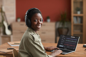 Portrait of female African-American musician using laptop and smiling at camera while composing...
