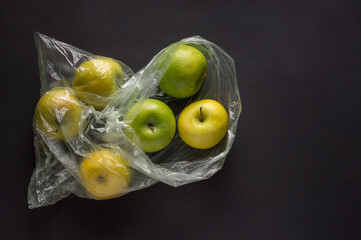 Transparent plastic crumpled cellophane bag with group of ripe green and yellow apples on a black background. Ecology concept