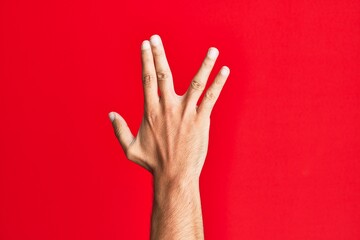 Arm of caucasian white young man over red isolated background greeting doing vulcan salute, showing back of the hand and fingers, freak culture