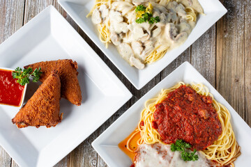 A top down view of several Italian entrees on a wooden table surface, featuring deep fried mozzarella, and spaghetti.