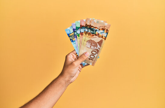 Hand of hispanic man holding one dollar banknote over isolated yellow background.
