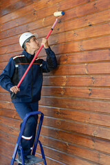 The painter varnishes the wooden wall. Wooden cottage maintenance