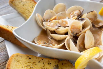 A view of a bowl of steamed clams, with garlic bread.