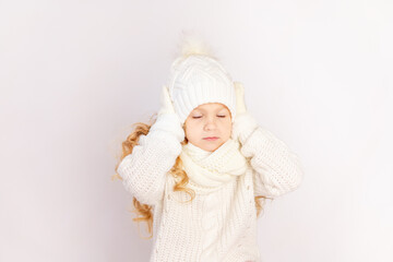 child girl in a sweater and hat holding her head with closed eyes on a white isolated background, space for text