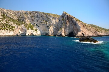 Fototapeta premium Limestone rocks on the coast of Zakynthos island, Greece. Sunny day, crystal clear water, blue sky, boat trip, rocks falling steeply into the sea.