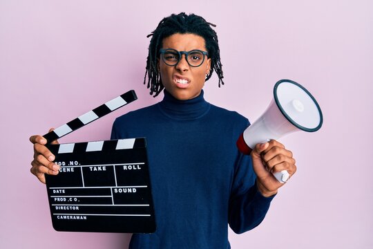 Young African American Man Holding Video Film Clapboard And Megaphone Clueless And Confused Expression. Doubt Concept.