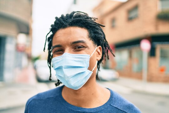 Young african american man wearing medical mask looking to the camera at street of city.