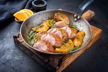 Traditional fried pork filet medaillons in with caramelized orange slices and herbs offered as close-up in a rustic wrought iron skillet - obrazy, fototapety, plakaty
