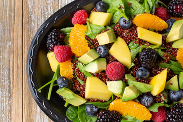 A top down view of a tropical salad, featuring spinach, fruit and quinoa.