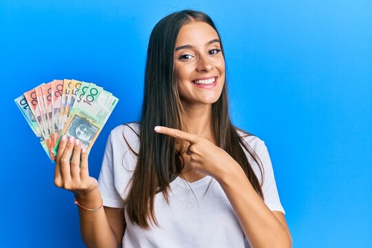 Young hispanic woman holding australian dollars smiling happy pointing with hand and finger