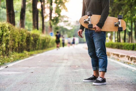 Closeup Asian man holding surfskate or skate board in outdoor Park when sunrise time over photo blur of unrecognized people running, extream sport, healthy and exercise, fashion in covid19 concept