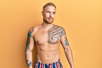 Fototapeta premium Young caucasian man wearing swimwear shirtless smiling looking to the side and staring away thinking.