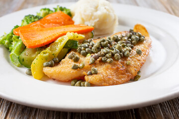 A view of a plate of fillet of white fish, in a restaurant or kitchen setting.